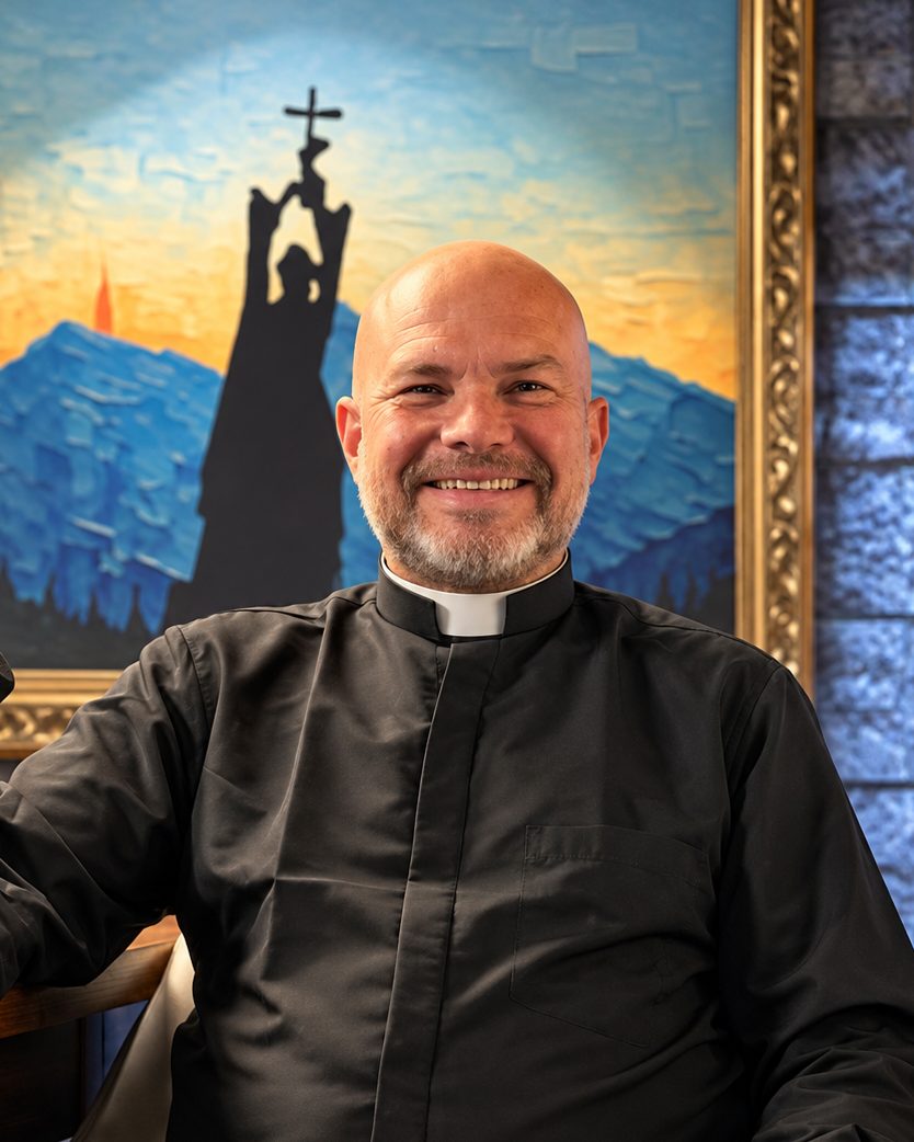 El Padre Iñigo López, sonriente, frente a una pintura de un caminante con la cruz en alto